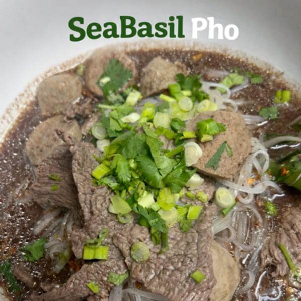 Close-up of Seabasil Pho with beef, meatballs, noodles, and green onions in a rich broth.