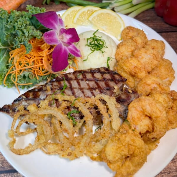 Grilled fish, fried shrimp, onion rings, mashed potatoes, and salad with a purple orchid garnish.